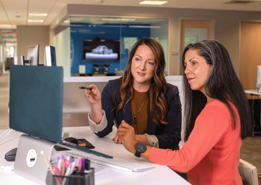 Two women sitting at a table in front of a computer.