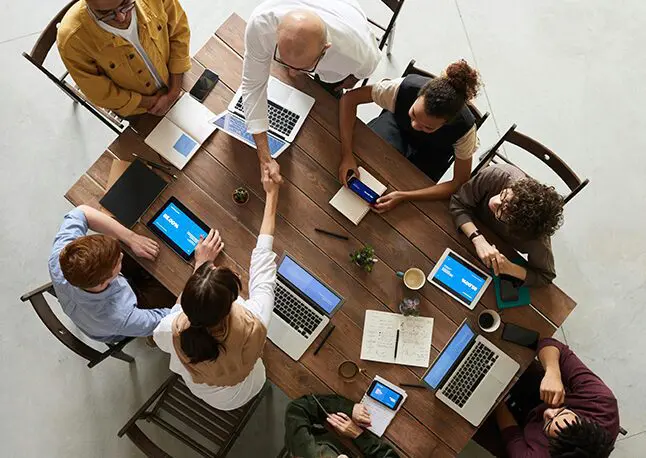 A group of people sitting around a table with laptops.